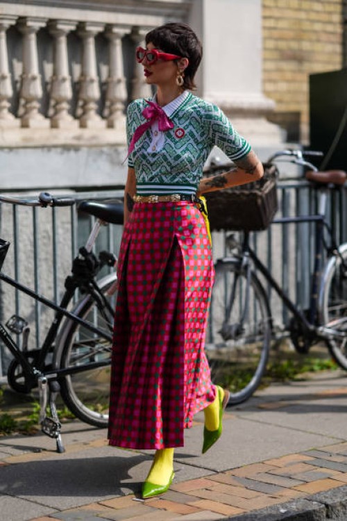 Guest wears red sunglasses, gold earrings, light green dark green pattern short sleeve shirt with hot pink bow, gold belt, dark pink hot pink green...