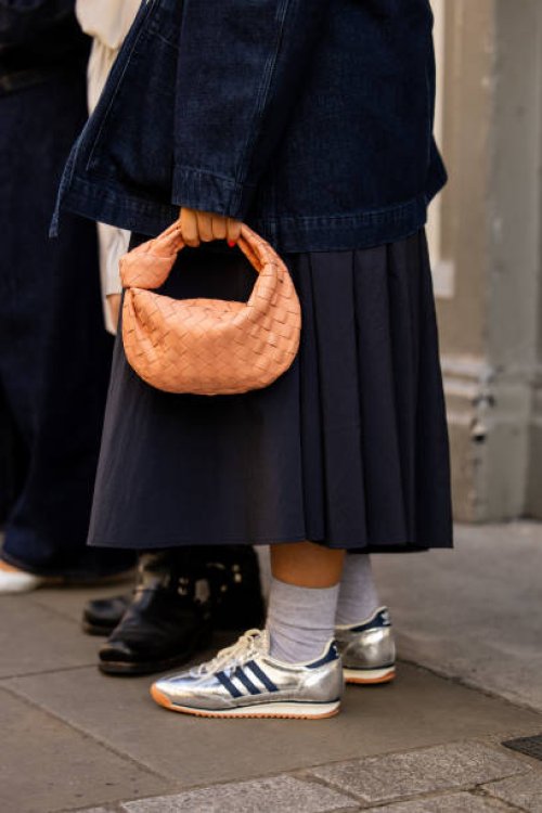 Guest wears salmon colored Bottega Veneta bag, silver Adidas sneaker outside Bora Aksu during London Fashion Week September 2024 on September 13,...