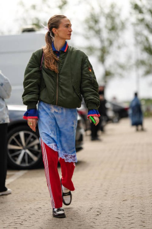 Guest wears silver earrings, a khaki nylon bomber coat, a pale blue and white tie and dye print pattern asymmetric knees dress, red with white...