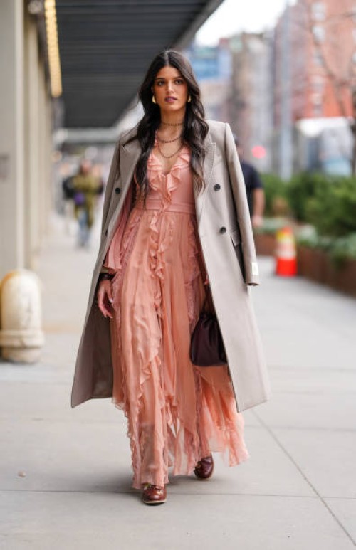 Guest wears silver earrings, black layered necklaces, light brown oversized blazer coat, light pink ruffled midi dress, shiny dark brown boots...