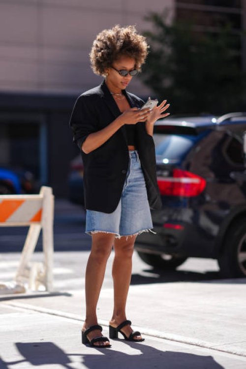 Guest wears silver earrings, black sunglasses, silver layered necklaces, black oversized blazer jacket, black bandeau top, washed light blue denim...