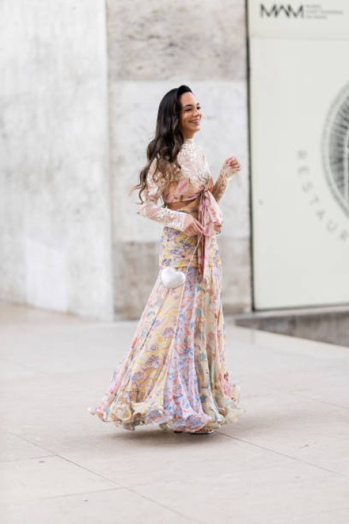 Guest wears silver heeled sandals, a white heart shaped bag and a floral long sleeved flounced long dress outside Zimmermann show during Womenswear...