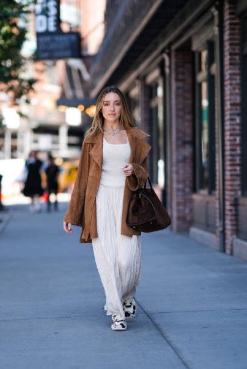 Guest wears silver layered necklaces, white pattern tank top, white flowy pants, light brown suede oversized jacket, dark brown suede bag, white...