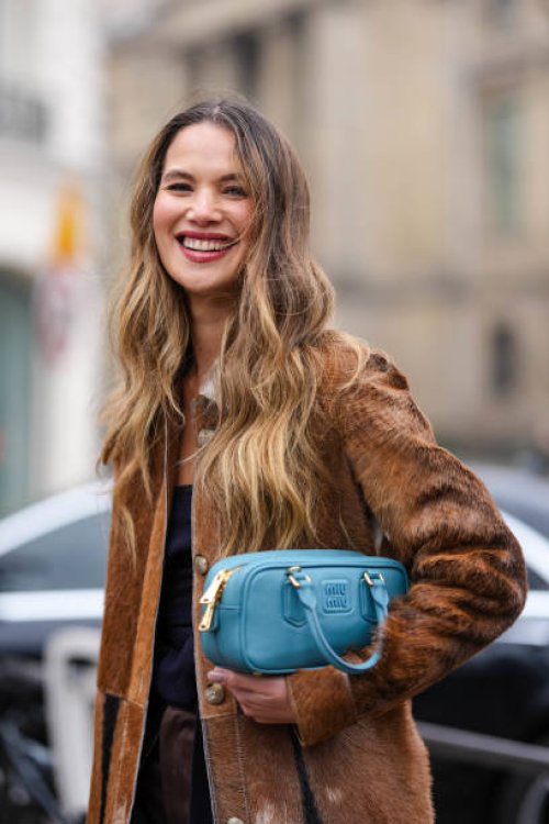 Guest wears silver necklace, black knit strapless Miu Miu top, dark brown faux fur coat, dark pink Miu Miu leather bag, outside Miu Miu, during the...