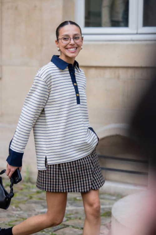 Guest wears striped polo shirt with long sleeves, skirt, bag, glasses outside Ganni during the Womenswear Fall/Winter 2025/2026 as part of Paris...