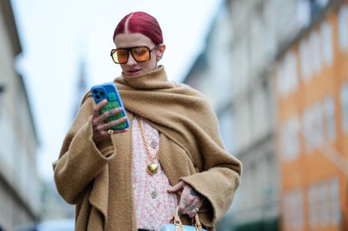 Guest wears sunglasses, a beige oversized long large fringed scarf, a matching long coat, pastel pink tweed jacket from Chanel, a blue bag from...