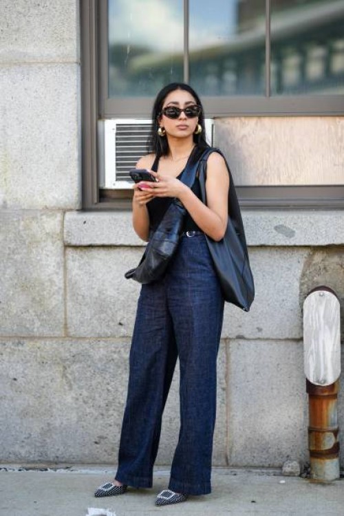 Guest wears sunglasses, a black tank top, blue denim jeans pants, a black leather bag, golden earrings, holds a mobile phone, outside Gabriela...