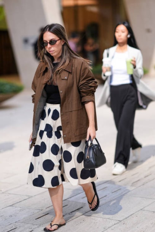 Guest wears sunglasses, a gray jacket, a black top, a black and white polka dots mini skirt , sandals, outside Toteme, during New York Fashion Week,...