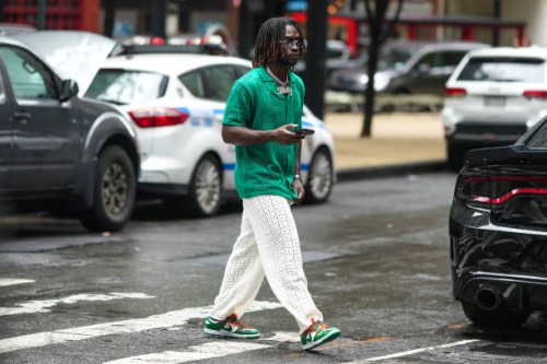 Guest wears sunglasses, a necklace a green shirt, white pants with floral embroidery, Nike green sneakers, outside Jason Wu, during New York Fashion...