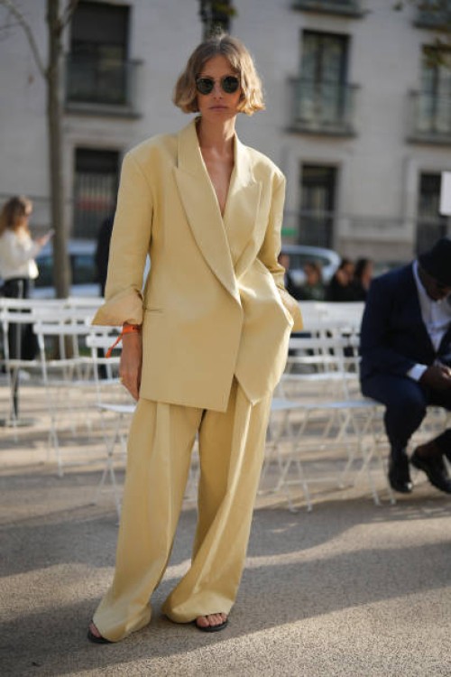 Guest wears sunglasses, a pale pastel yellow oversized blazer jacket, matching flared pants, before Stella McCartney, during the Womenswear...