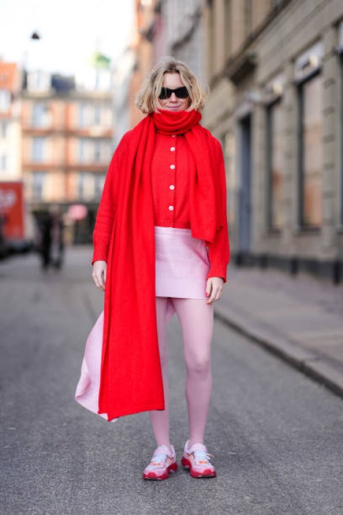 Guest wears sunglasses, a red oversized long scarf, a red cardigan, a pink mini skirt, tights, red and pink sneakers shoes , outside Mark Kenly...