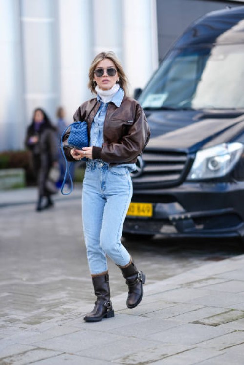 Guest wears sunglasses, a white turtleneck pullover, a blue denim shirt, a blue woven leather bag, blue denim jeans pants , brown leather boots...