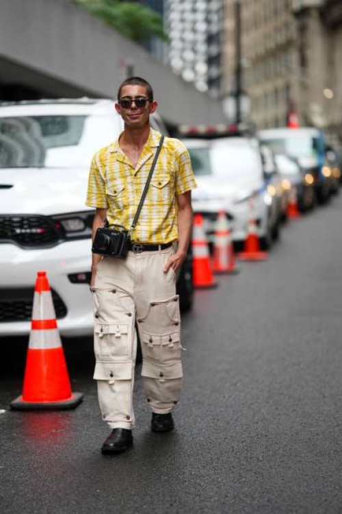 Guest wears sunglasses, a yellow and white checkered shirt, a camera in a leather camera bag, a Telfar belt, beige trousers, black leather shoes,...