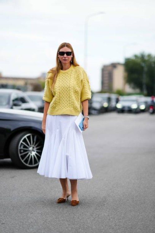 Guest wears sunglasses, earrings, a yellow knit pullover, a white godet midi skirt, brown suede pointy mules, outside Prada, during the Milan Fashion...