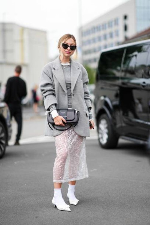 Guest wears sunglasses, necklaces, a grey pullover, a grey fluffy jacket, a two-tone Prada bag, a sequined white transparent lace midi skirt, white...