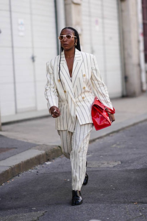 Guest wears white glasses, earrings, rings, an oversized double-breasted white jacket with thin black stripes, matching large pants, black leather...