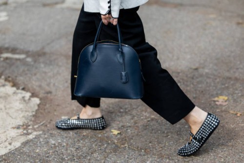 Guest wears white jacket, black skirt, Alaia shoes, navy bag outside Ferragamo during the Milan Fashion Week Menswear Spring/Summer 2025 on September...