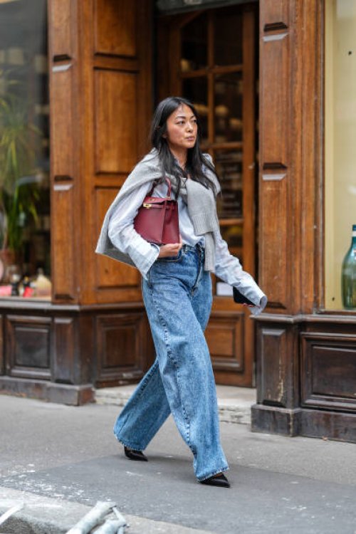 Guest wears white linen buttoned up long sleeve shirt, light gray sweater wrapped around shoulders, dark red Hermes Birkin leather bag, acid washed...