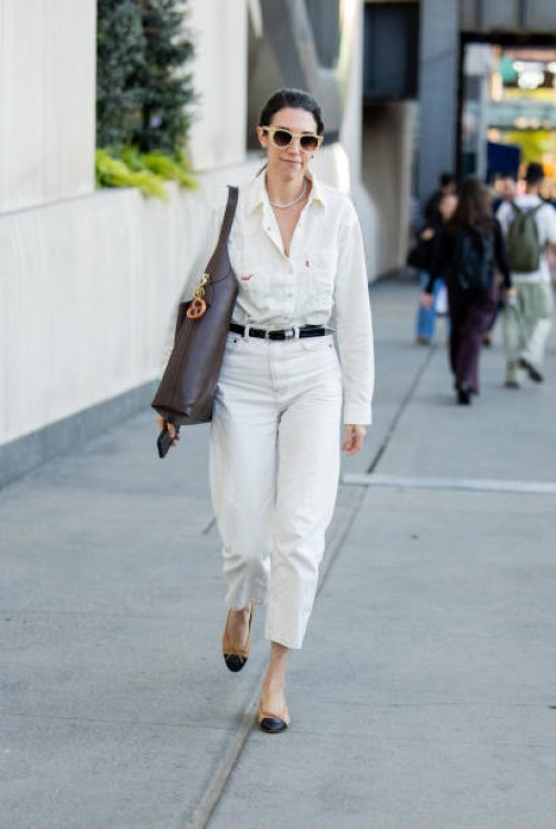 Guest wears white pants, shirt, brown bag outside Michael Kors during New York Fashion Week on September 10, 2024 in New York City.
