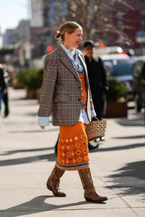 Guest wears white pearls earrings, a white embroidered pearls large necklace, a pale blue shirt, an orange wool cut-out pattern with brown and blue...