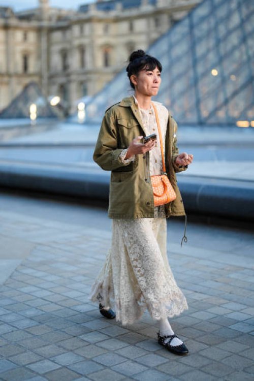 Guest wears white sheer mesh lace midi dress, bright orange bag, dark green oversized jacket, white socks, black ballerina flats leather shoes,...