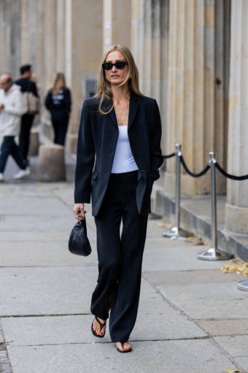 Guest wears white shirt, black blazer, striped pants, sunglasses, sandals outside Horror Vacui during the Berlin Fashion Week SS25 on July 03, 2024...