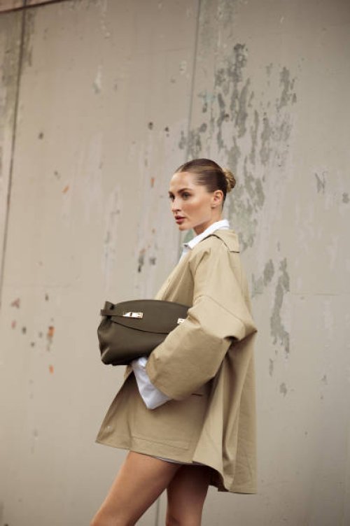 Guest wears white shirt, white skirt, beige coat and olive green bag outside Ferragamo show during the Milan Fashion Week Spring/Summer 2025 on...