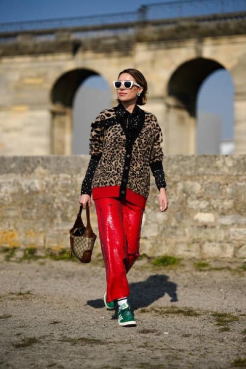 Guest wears white sunglasses, crystals and emerald pendant earrings, a black with white polka dots print pattern blouse, a black buttoned wool...