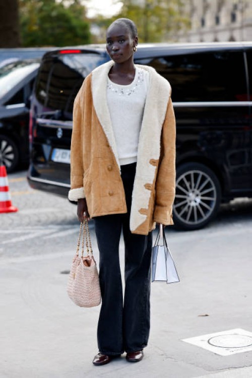 Guest wears white sweater, black jeans, beige suade jacket with cream fur details, outside Chanel, during Womenswear Spring/Summer 2025 as part of...