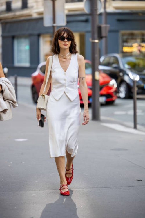 Guest wears white vest, silk skirt, red heels outside RDNT Andre Tan during the Womenswear Spring/Summer 2024 as part of Paris Fashion Week on...