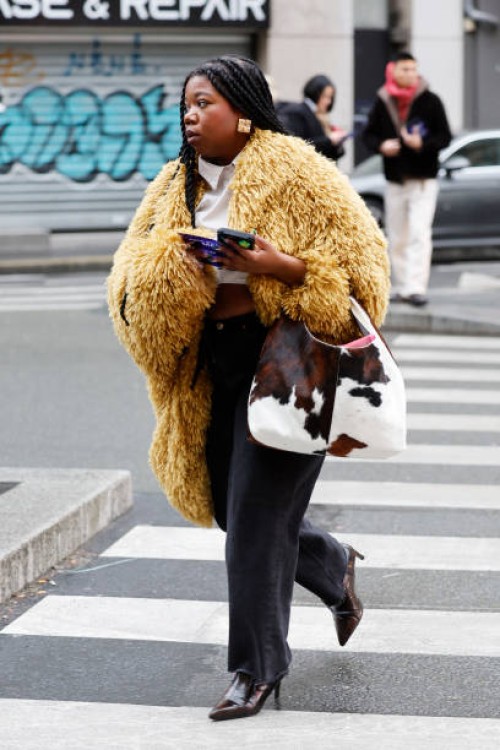 Guest wears yellow fur jacket, white cropped shirt, black jeans, brown boots, cow print bag, outside Junya Watanabe, during the Menswear Fall Winter...