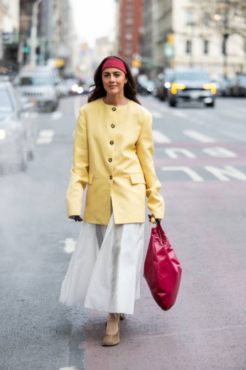 Guest wears yellow jacket, red head band, bag, white skirt outside Altuzarra during New York Fashion Week on February 08, 2025 in New York City.