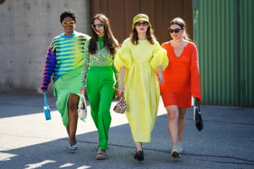 Guest wears yellow sunglasses, gold earrings, gold chain pendants necklaces, a black with multicolored print pattern wool pullover, a green ribbed...