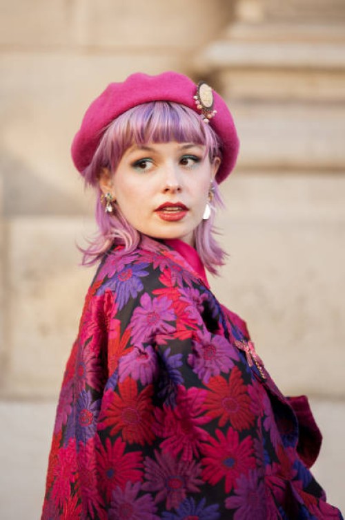 Guest with pink hair is seen wearing red, pink, purple and black flower pattern jacket, matching color checkered skirt, pink beret and pink bag...