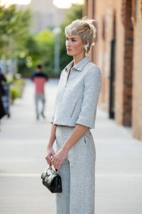 Guest with short hair cut wears grey jacket, pants, black bag outside Tory Burch during New York Fashion Week on September 09, 2024 in New York City.