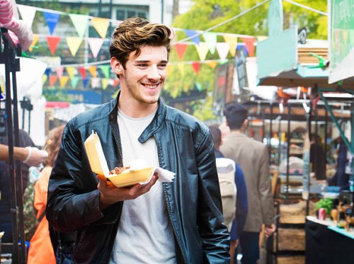handsome british man walks through fair market with street food - food stock pictures, royalty-free photos & images