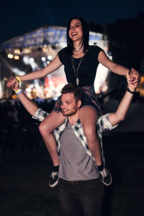 handsome guy holding a cute girl friend on his shoulders. stage glowing in the bakcground - concert stock pictures, royalty-free photos & images