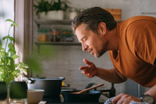 handsome young man enjoying the aroma of a meal in a kitchen - food stock pictures, royalty-free photos & images