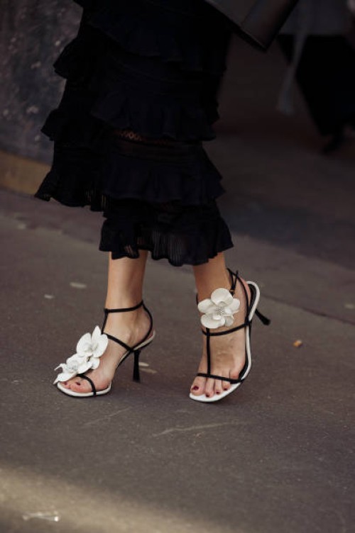 Hanneli Mustaparta is seen wearing a black tailored blazer, black ruffled skirt, long bag, heeled sandals with flower, and sunglasses outside...