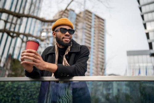 happy american guy holding take away coffee and looking into distance while walking in urban area - coffee stock pictures, royalty-free photos & images