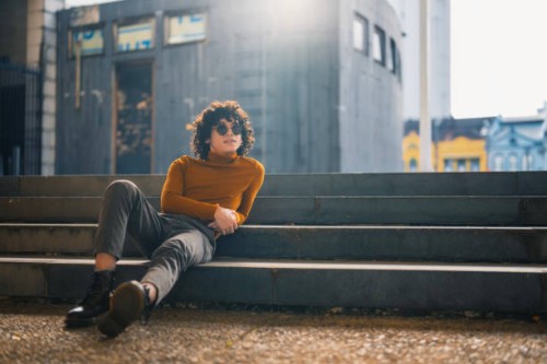 happy asian malay young man looking away sitting on ground with backlit sunlight in city street - fashion stock pictures, royalty-free photos & images
