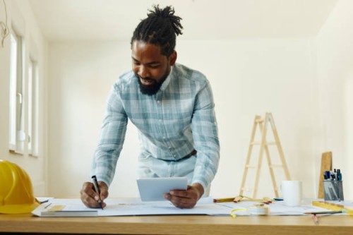 happy black architect using touchpad while examining plans in the apartment. - home decoration stock pictures, royalty-free photos & images