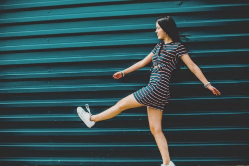 happy brunette young woman walking on street against blue wall - fashion stock pictures, royalty-free photos & images