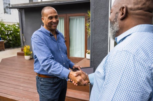 happy businessman shaking hands with male customer while standing outside house - home decoration stock pictures, royalty-free photos & images