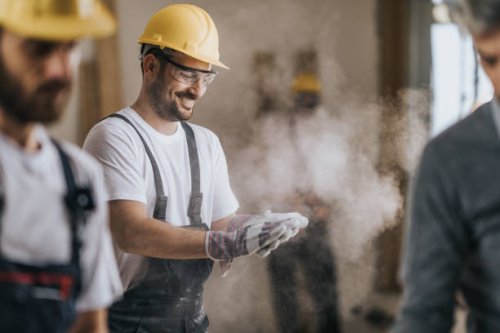 happy construction worker cleaning his gloves from sawdust at in renovating apartment. - home decoration stock pictures, royalty-free photos & images