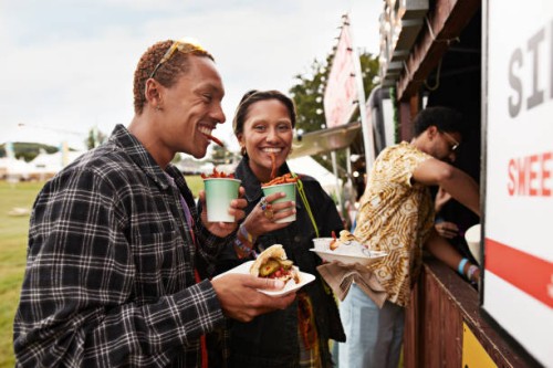 happy couple eating street food by concession stand - junk food stock pictures, royalty-free photos & images