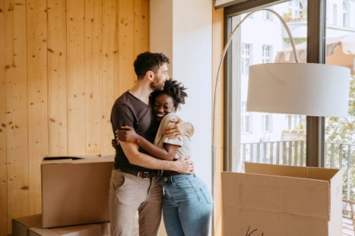 happy couple embracing each other while standing near window at new home - home decoration stock pictures, royalty-free photos & images