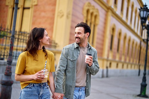 happy couple holding hands and drinking coffee while walking down the street - junk food stock pictures, royalty-free photos & images
