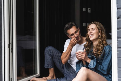 happy couple in nightwear at home sitting at french window - coffee stockfoto's en -beelden