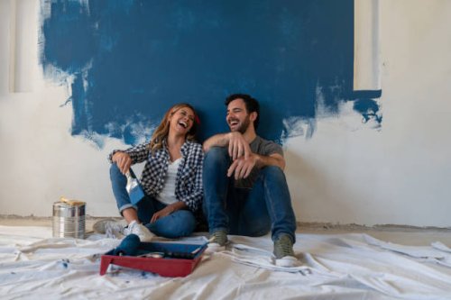 happy couple laughing while taking a break from painting - home decoration stock pictures, royalty-free photos & images